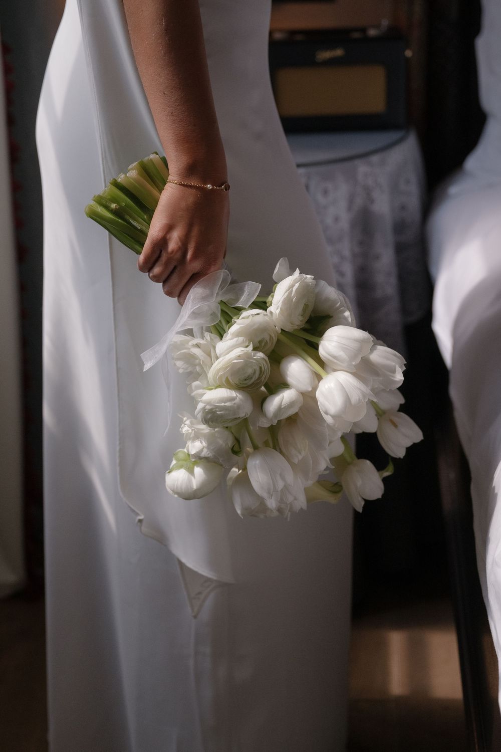 Close-up of white tulip bouquets held against white dresses in elegant wedding setting.