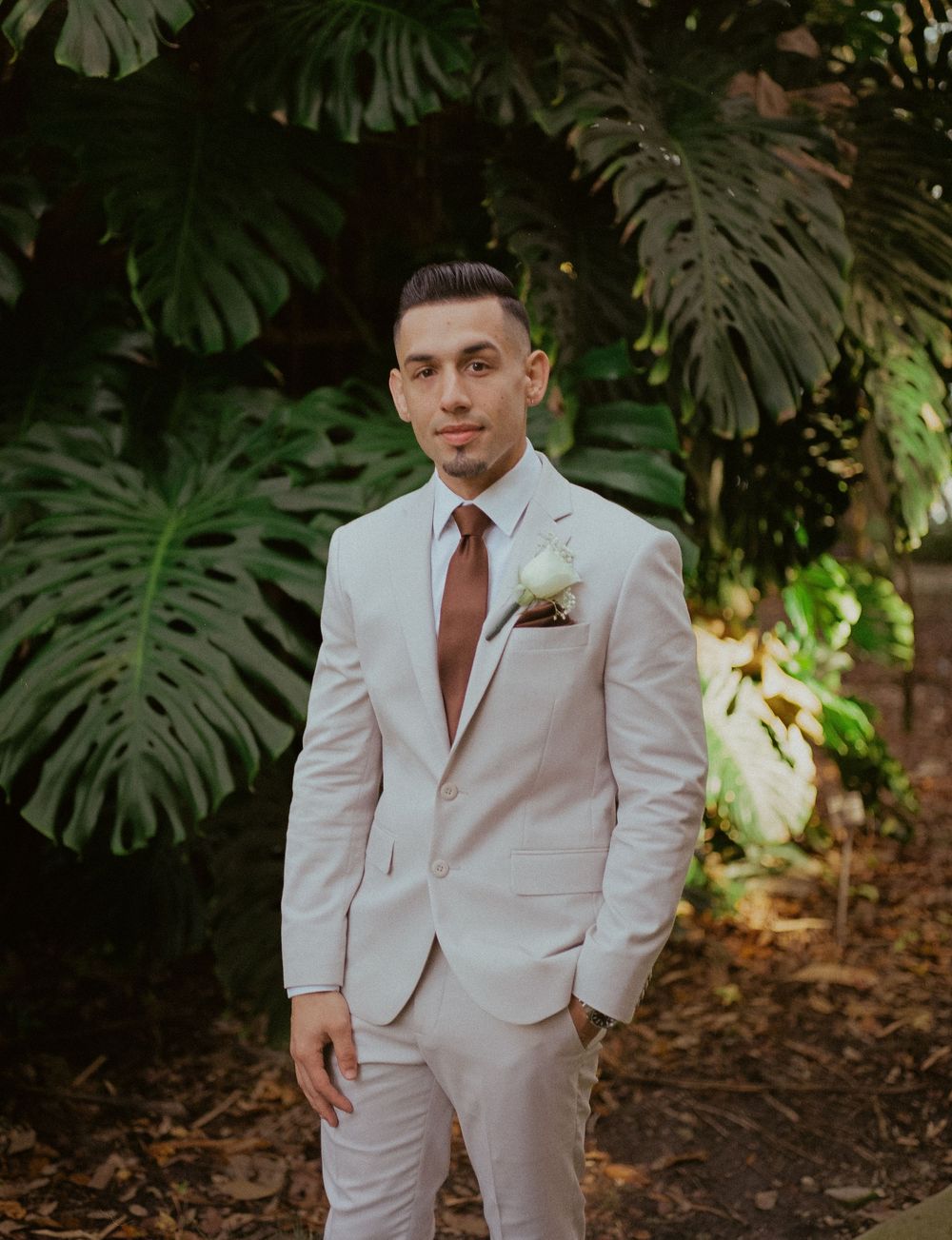 Elegant beige suit against a backdrop of tropical monstera leaves in a garden setting.
