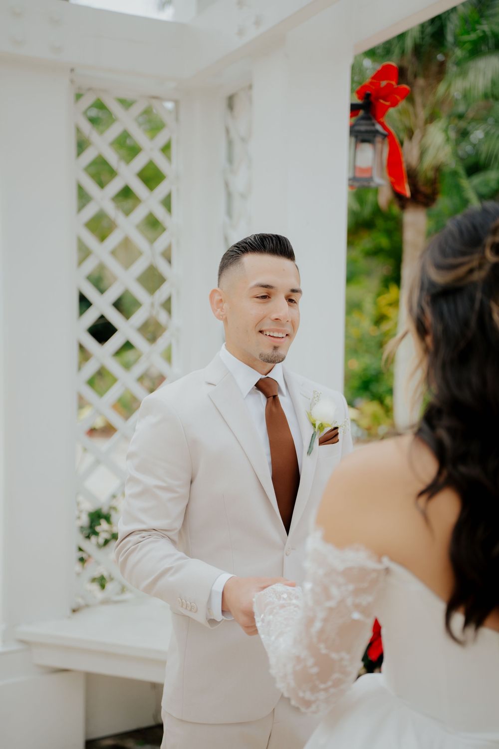 A romantic wedding scene in a white gazebo with lattice details and lush greenery in the background.