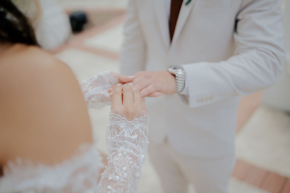 Close-up shot of delicate white lace and beading details on a wedding dress being adjusted by hands in soft lighting.