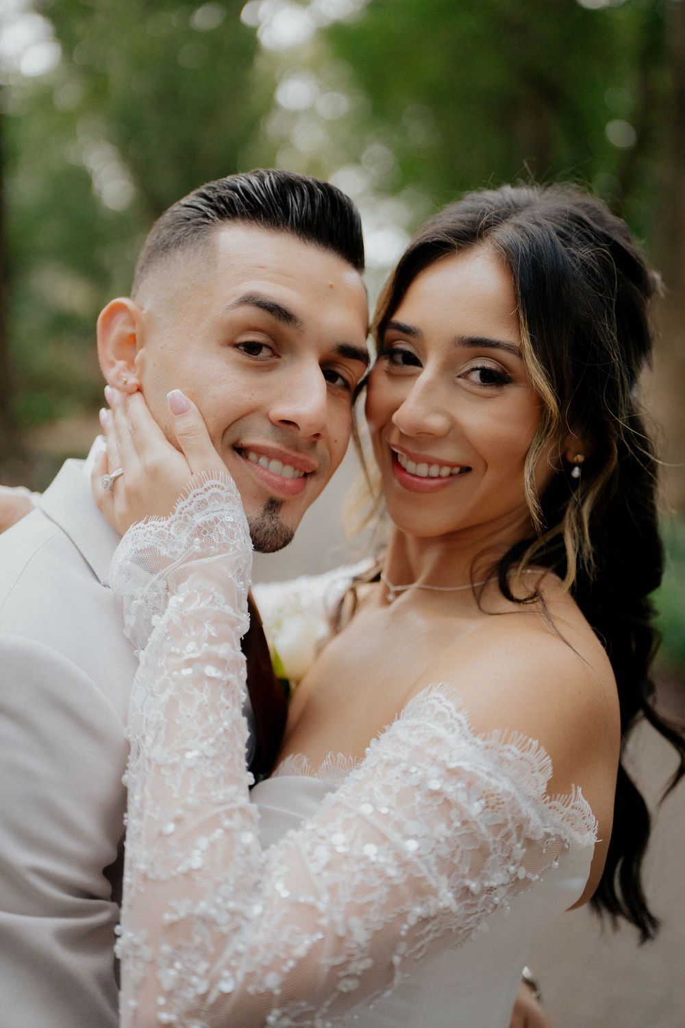 An intimate wedding portrait captured against a natural outdoor backdrop with soft bokeh lighting effects.