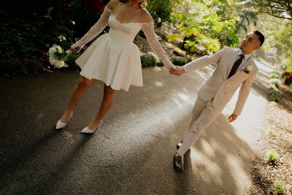Dancing couple in wedding attire twirling on a garden path.