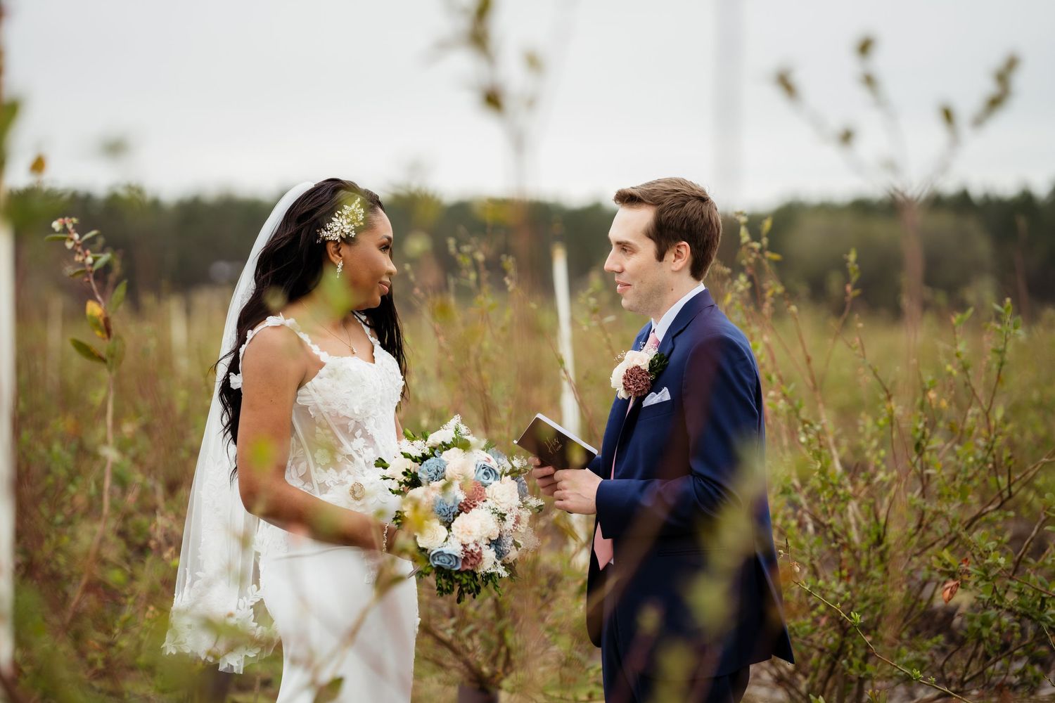A bride and groom share an intimate moment together in a rustic outdoor field at sunset.