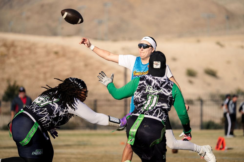 A flag football quarterback initiates a pass while a rusher attempts to pull their flags at the Sin City Classic tournament hosted by NGFFL