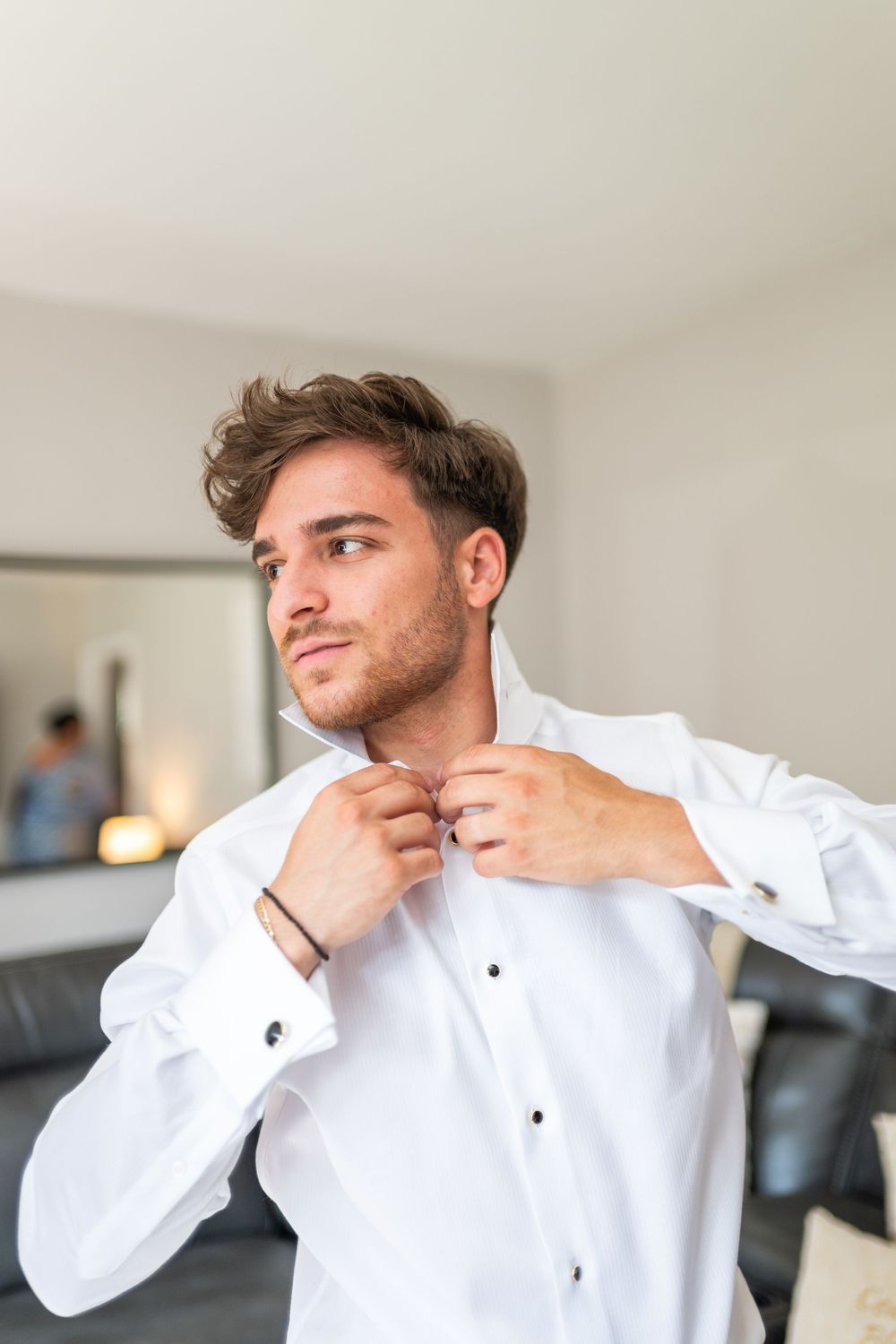 Someone buttons up a crisp white dress shirt while getting ready in a modern interior space.