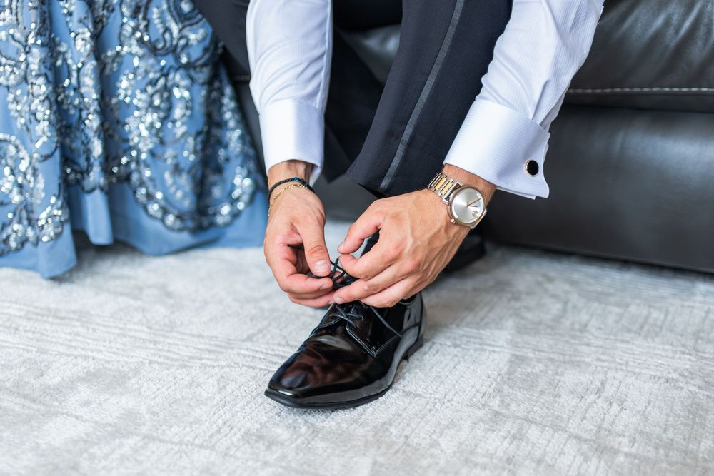 Close-up view of hands tying black leather dress shoes on gray concrete floor.