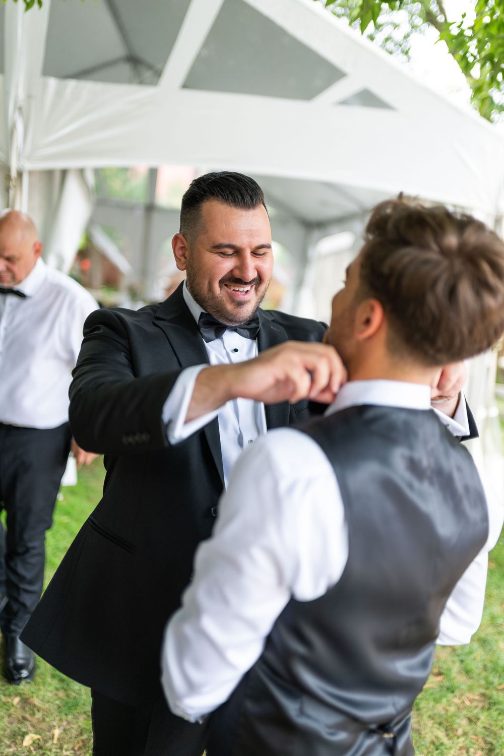 Two people in formal attire share a joyful moment under a white tent canopy at an outdoor event.