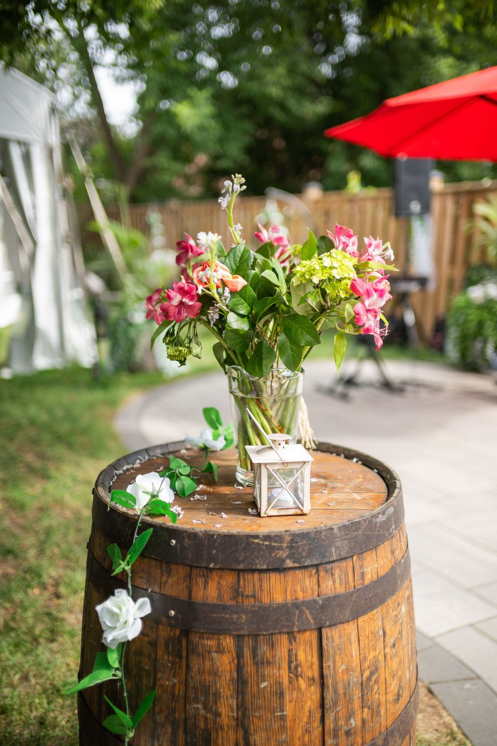 A rustic wooden barrel decorated with pink and white flowers serves as an outdoor planter along a garden pathway.