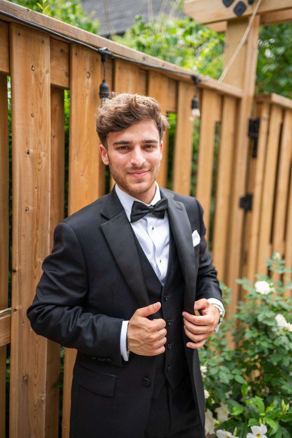 A series of photos showing someone in a black tuxedo and bow tie posing against a wooden fence in a garden setting.