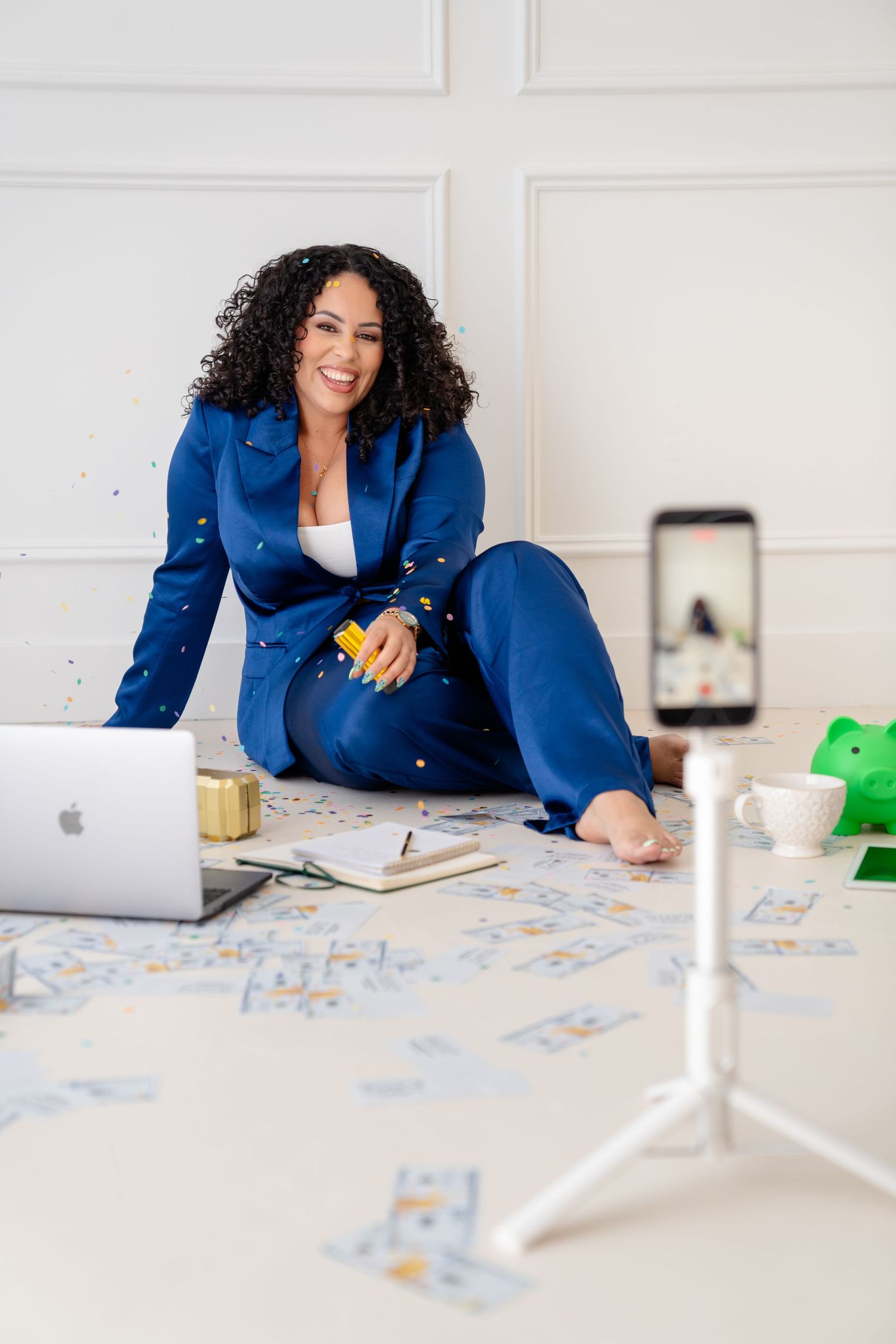 Professional wearing a bright blue blazer sits at a white desk with papers spread out while working on a laptop.
