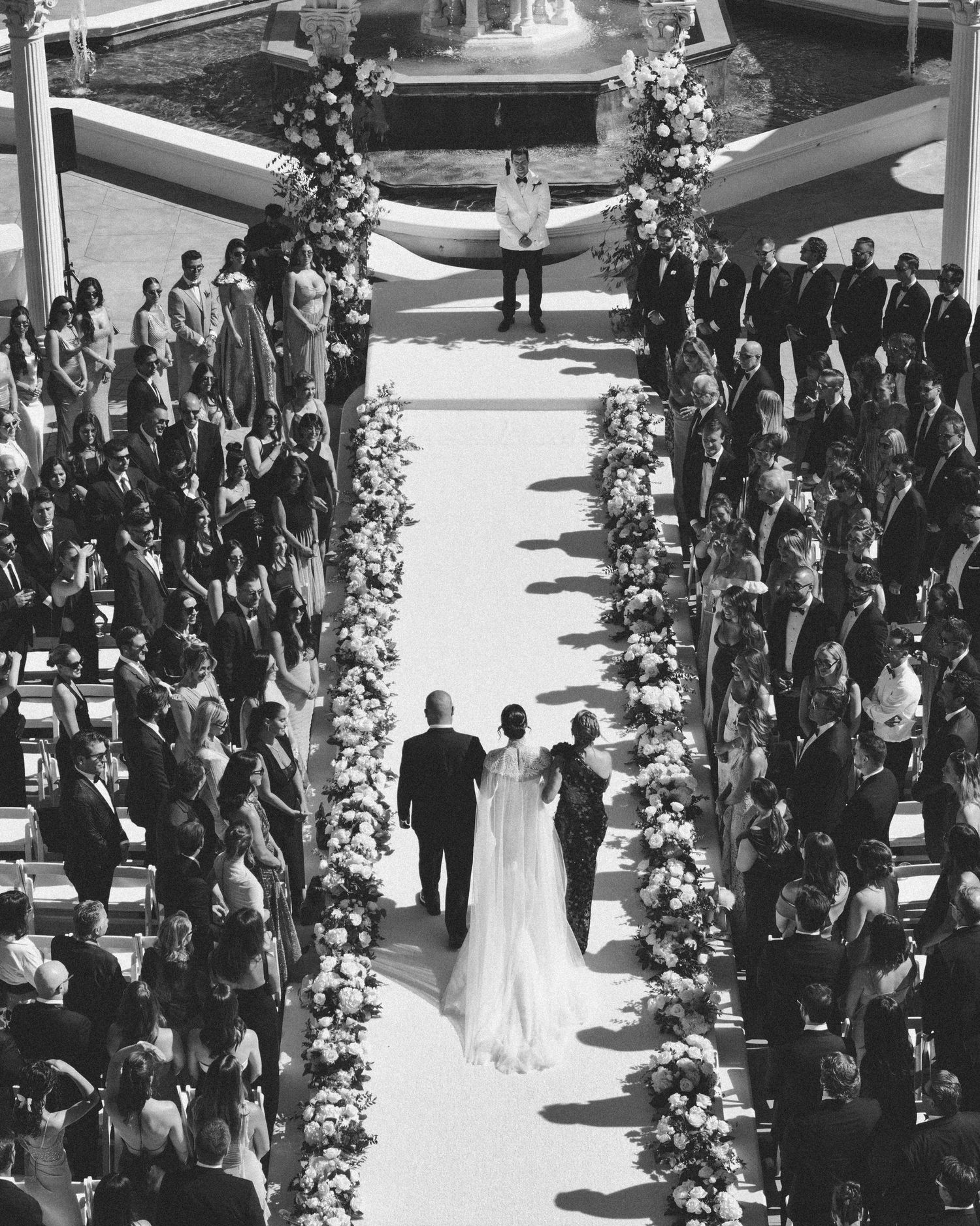 Black and white aerial view of an outdoor wedding ceremony with guests seated in rows around a central aisle.