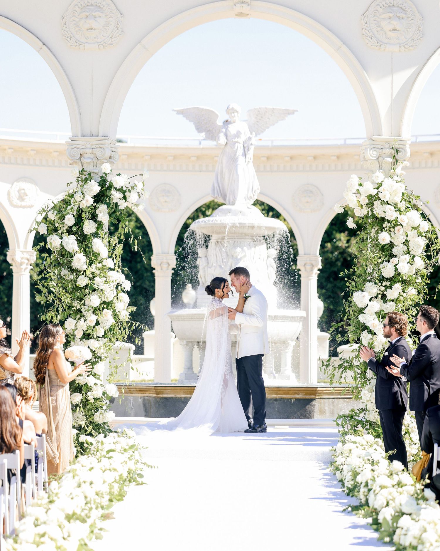 Elegant wedding ceremony in white arched courtyard with floral arrangements and angel fountain centerpiece.