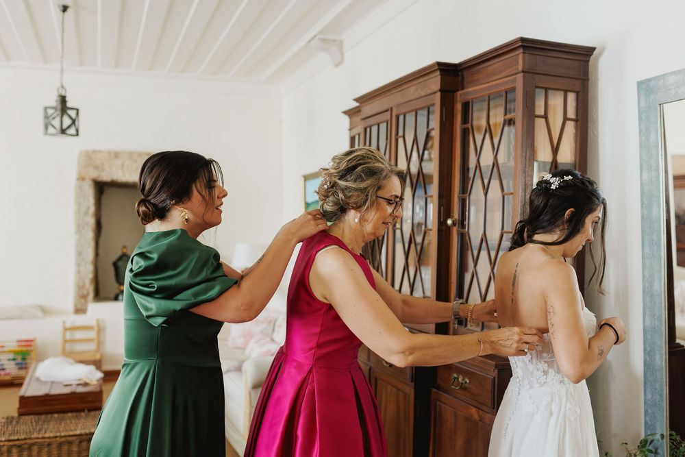 bride getting into wedding dress with help from mother and bridesmaid