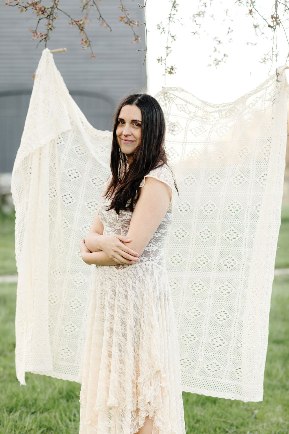 A mother with brown hair wears a cream lace dress with cream crochet blanket in background for motherhood portraits in Concord, MA