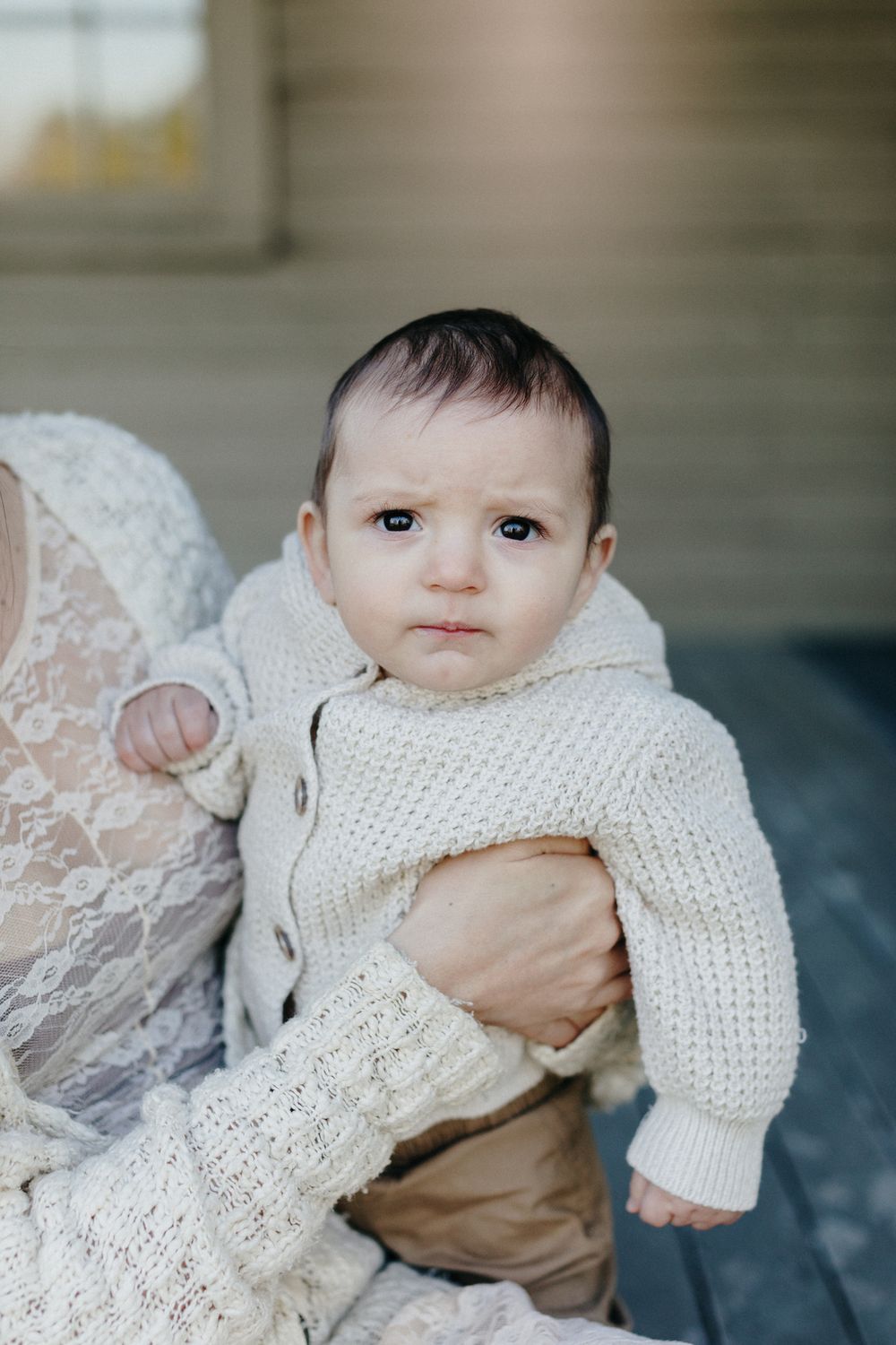 A baby boy wearing a cream sweater looks at the camera during a motherhood photo shoot in Middlesex County Lincoln, Massachusetts