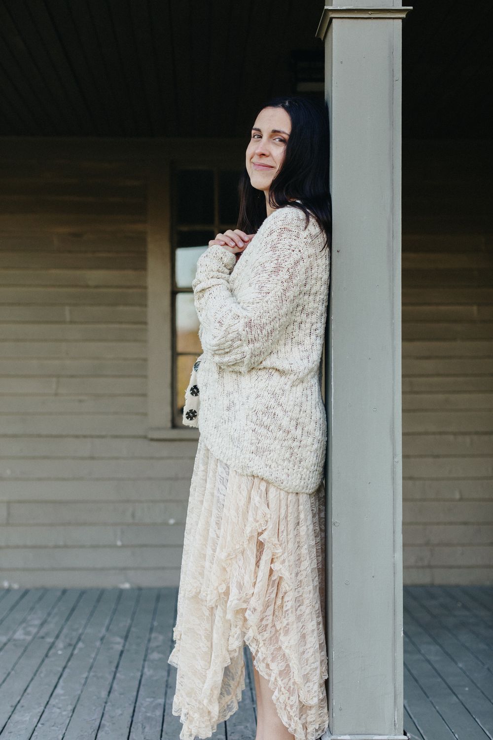 A portrait of a mother leaning on a weathered porch post at the Buttricks House in Concord, MA during a motherhood photo shoot.