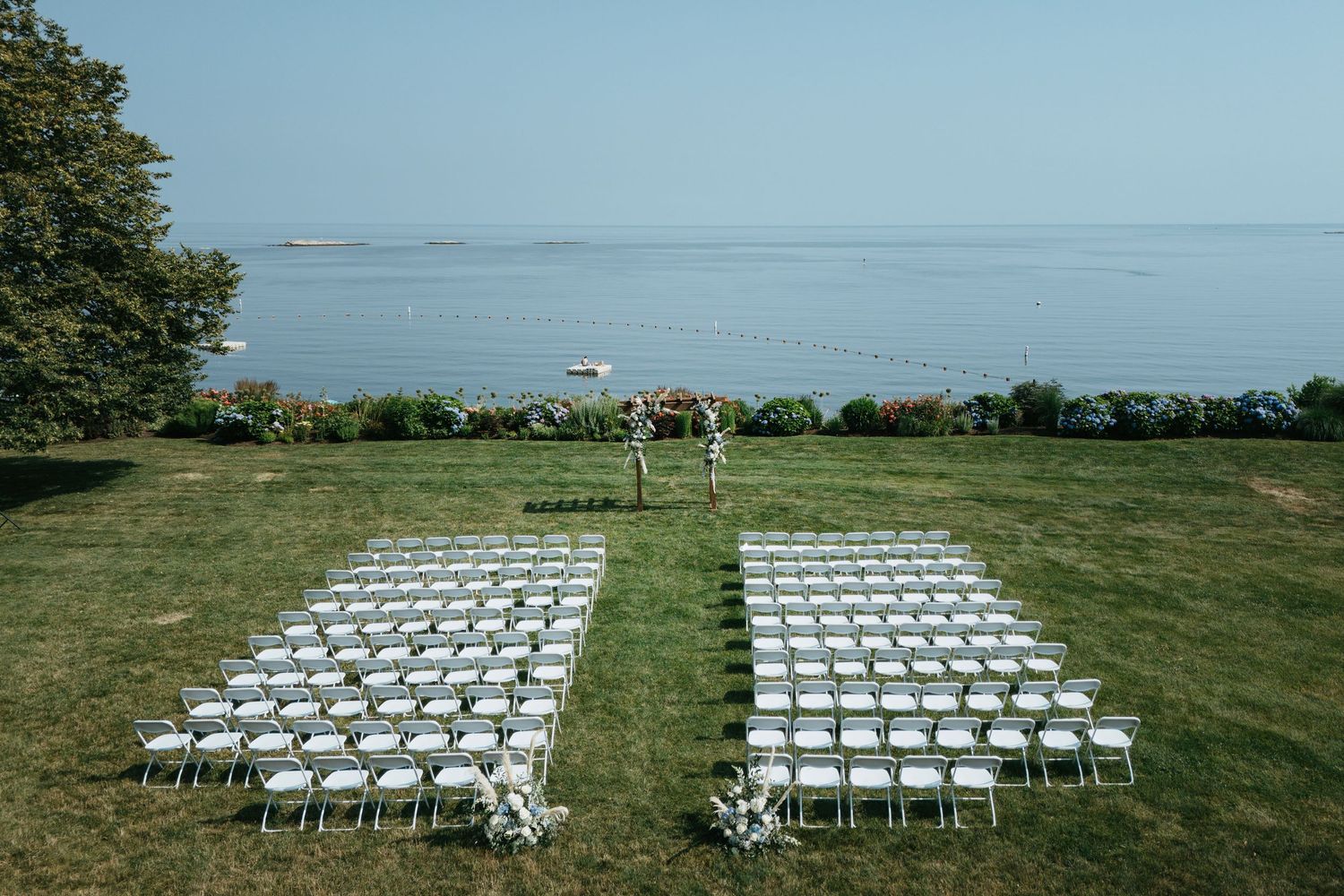 Aerial view of white chairs arranged in rows on a lush green lawn for an outdoor wedding ceremony.