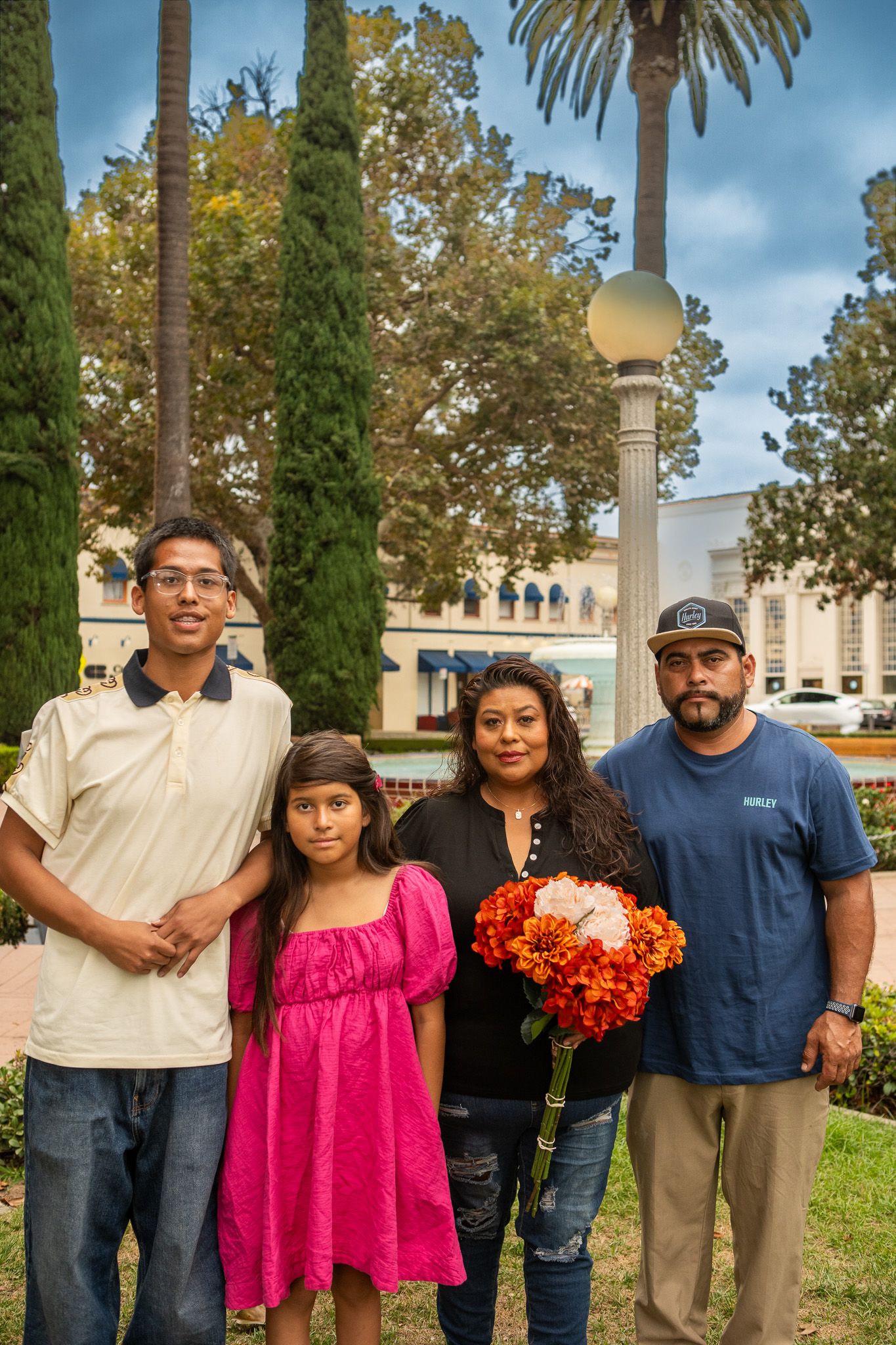 A family poses together outdoors with palm trees and ornate architecture visible in the background.