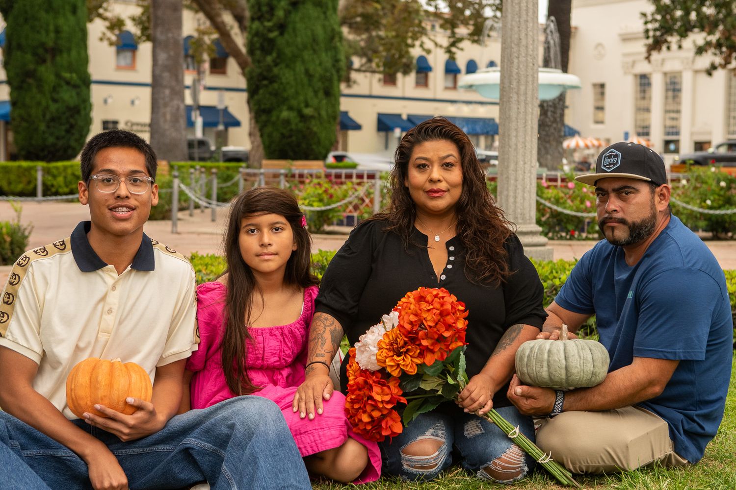 A group sits outdoors with autumn decorations including pumpkins and orange flowers in a garden setting.