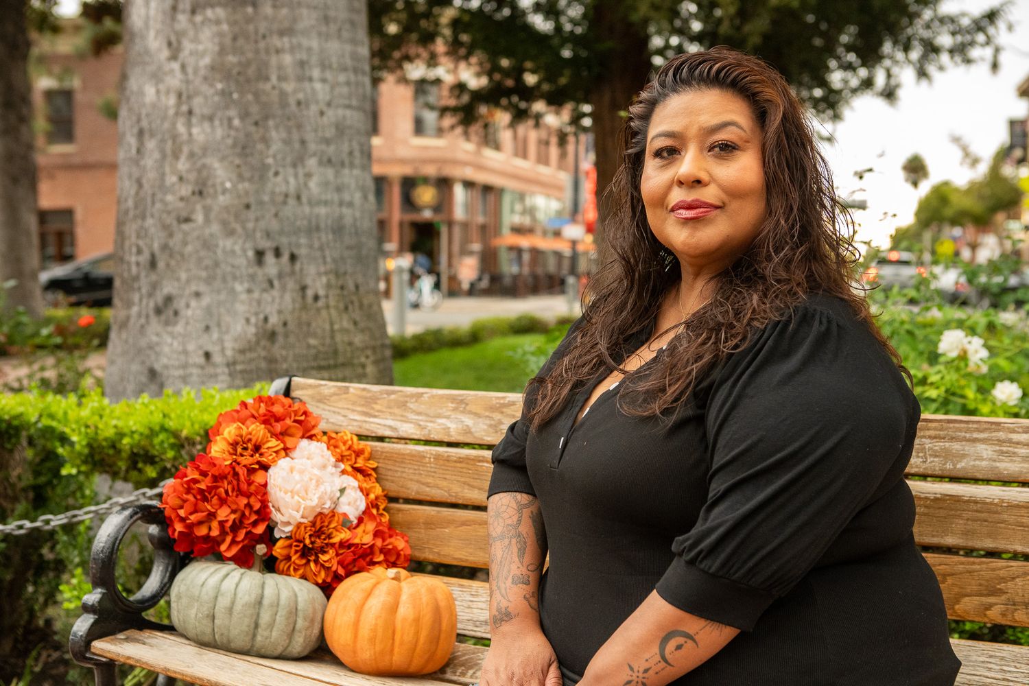 A casual outdoor scene with people seated on wooden benches surrounded by autumn decor and pumpkins.