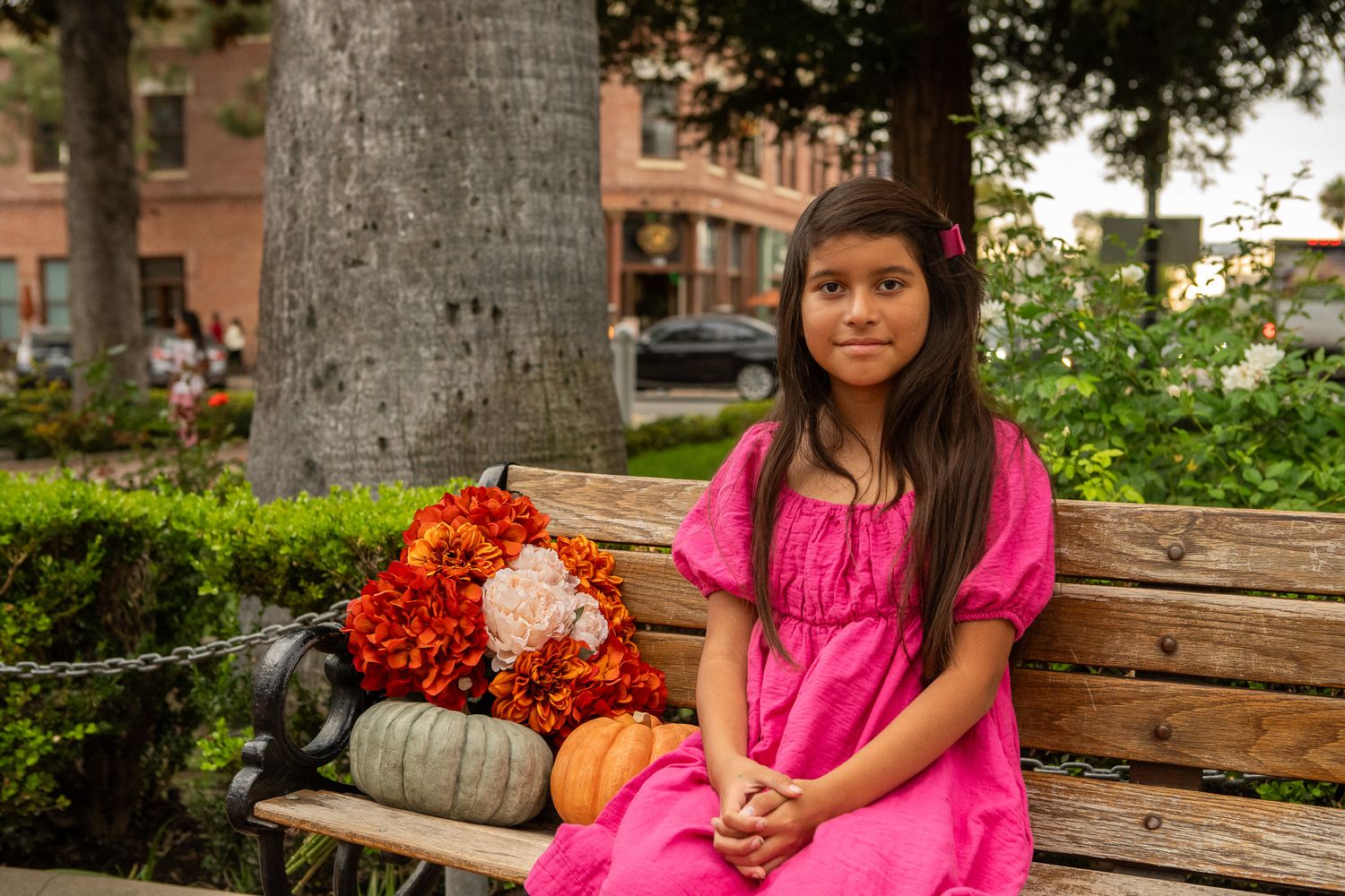 A bright pink dress stands out against a rustic wooden bench setting with fall decorations.
