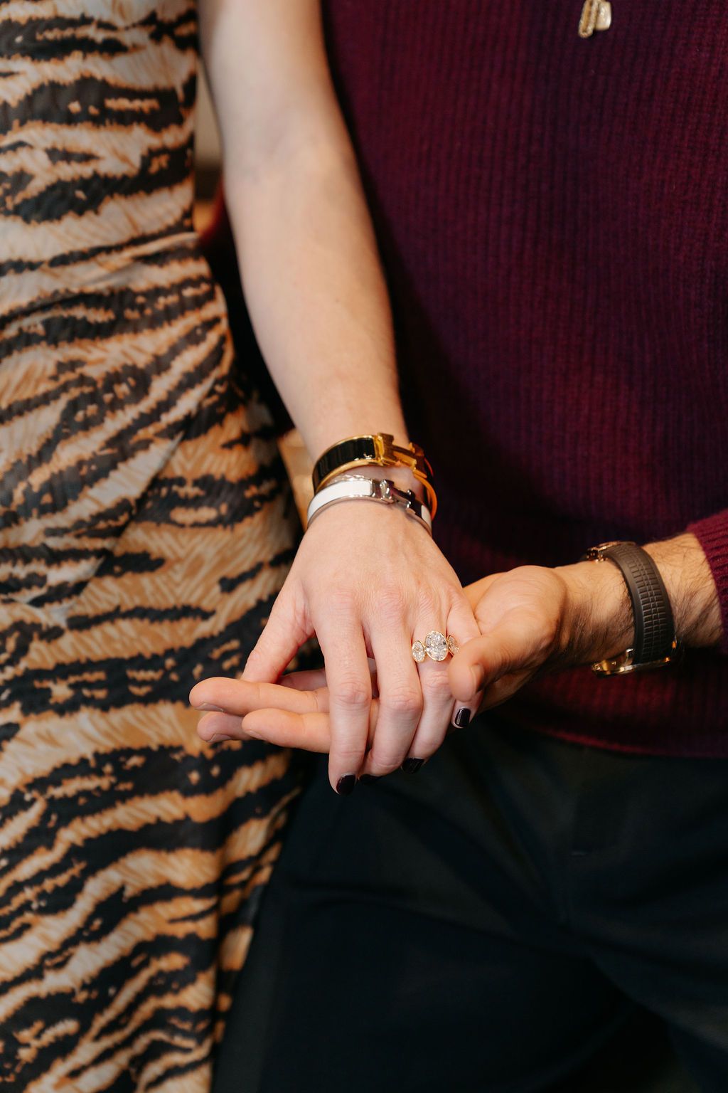 Close-up of hands wearing burgundy sweater showing engagement ring with tiger print fabric in background.