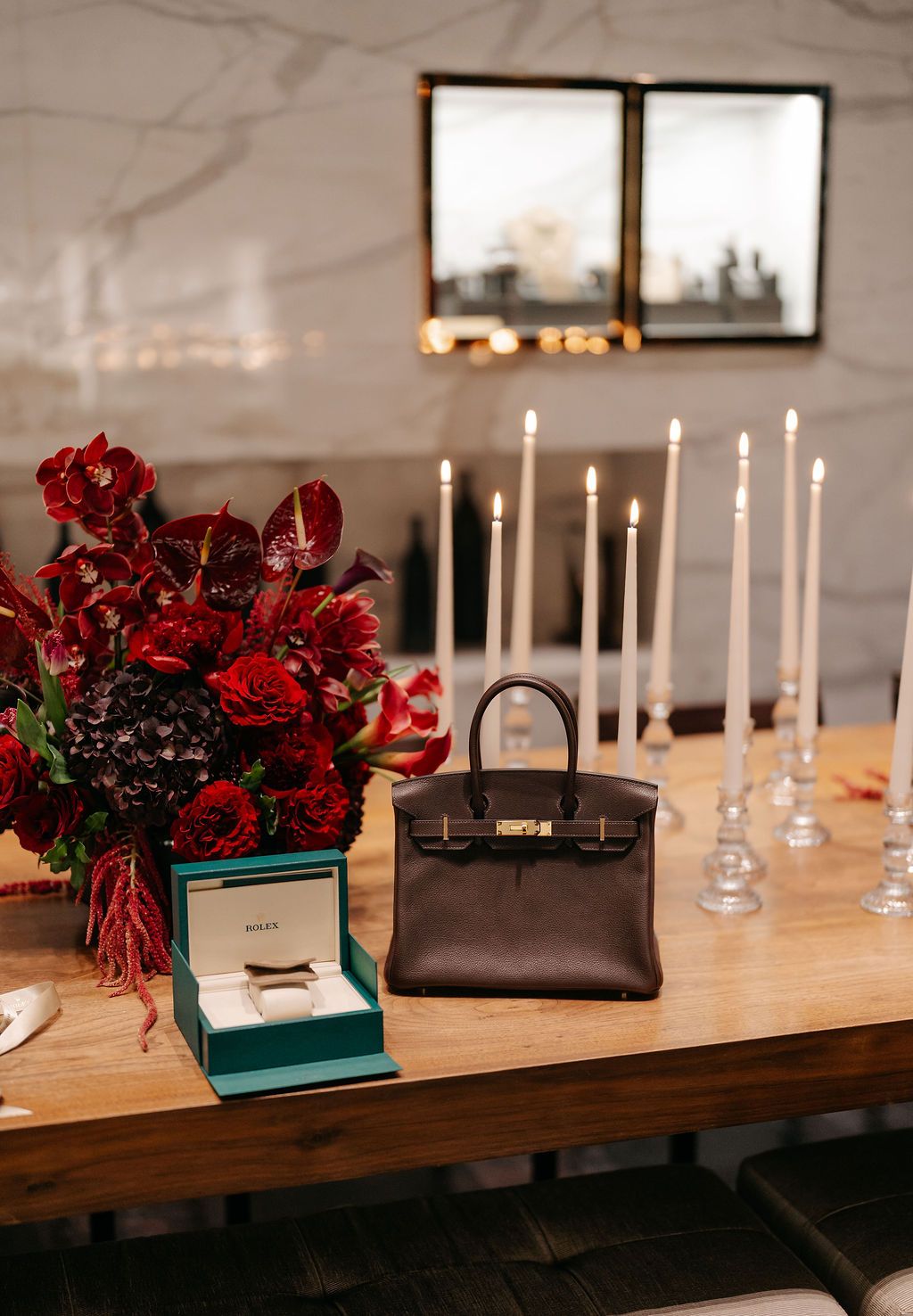 Elegant table setting with red floral arrangements, white candles, and teal accents on a wooden surface.