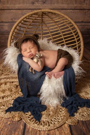 newborn wearing bear hat in rattan egg chair prop and jute rug