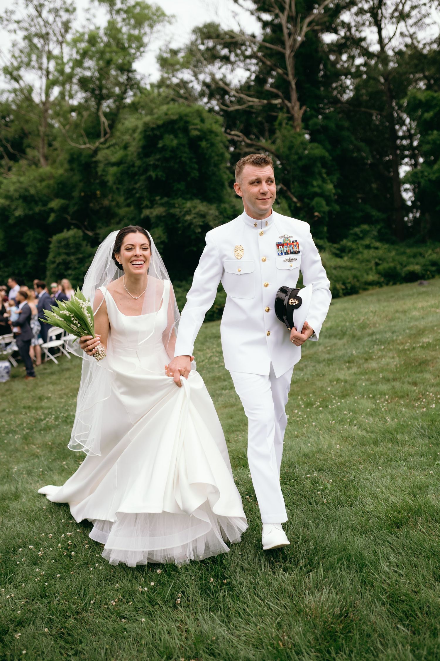 An outdoor wedding ceremony shows guests seated in white chairs as a couple shares their first kiss as newlyweds.