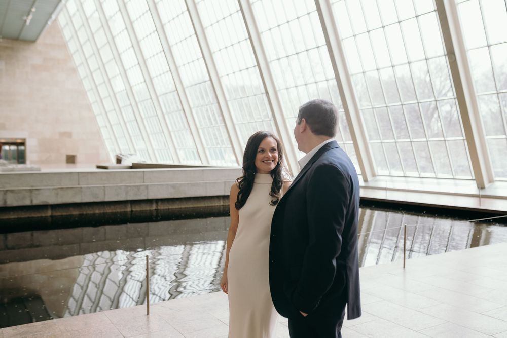 A couple stands in a modern architectural space with dramatic angular windows and reflective surfaces.