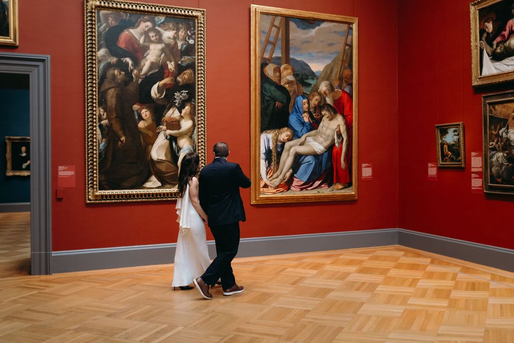 Art museum gallery with red walls displaying classical paintings.