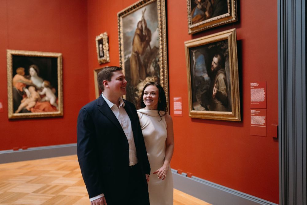 Couple admiring artwork on red walls in an art gallery or museum exhibition space.