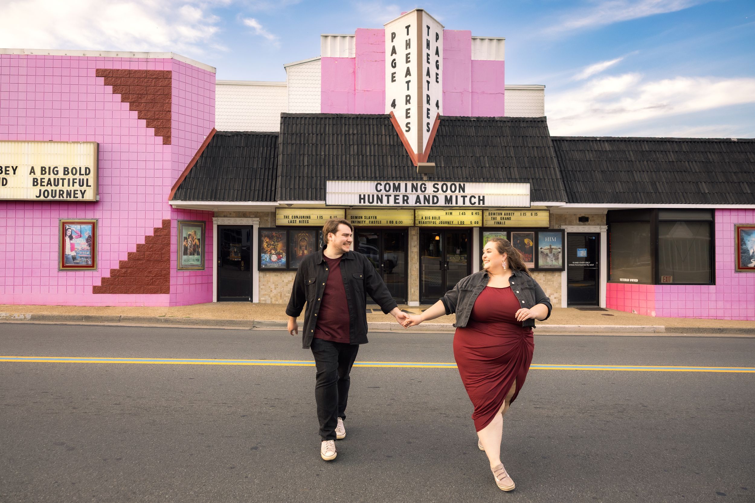 People walking past a retro-style pink building facade under a blue sky with white clouds.