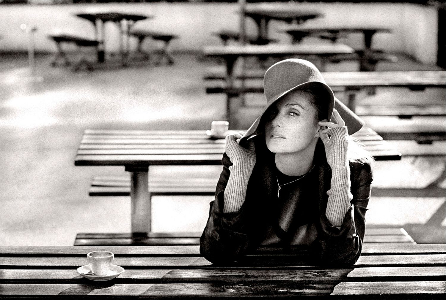A black and white photo of someone in a wide-brimmed hat sitting contemplatively at a picnic table.