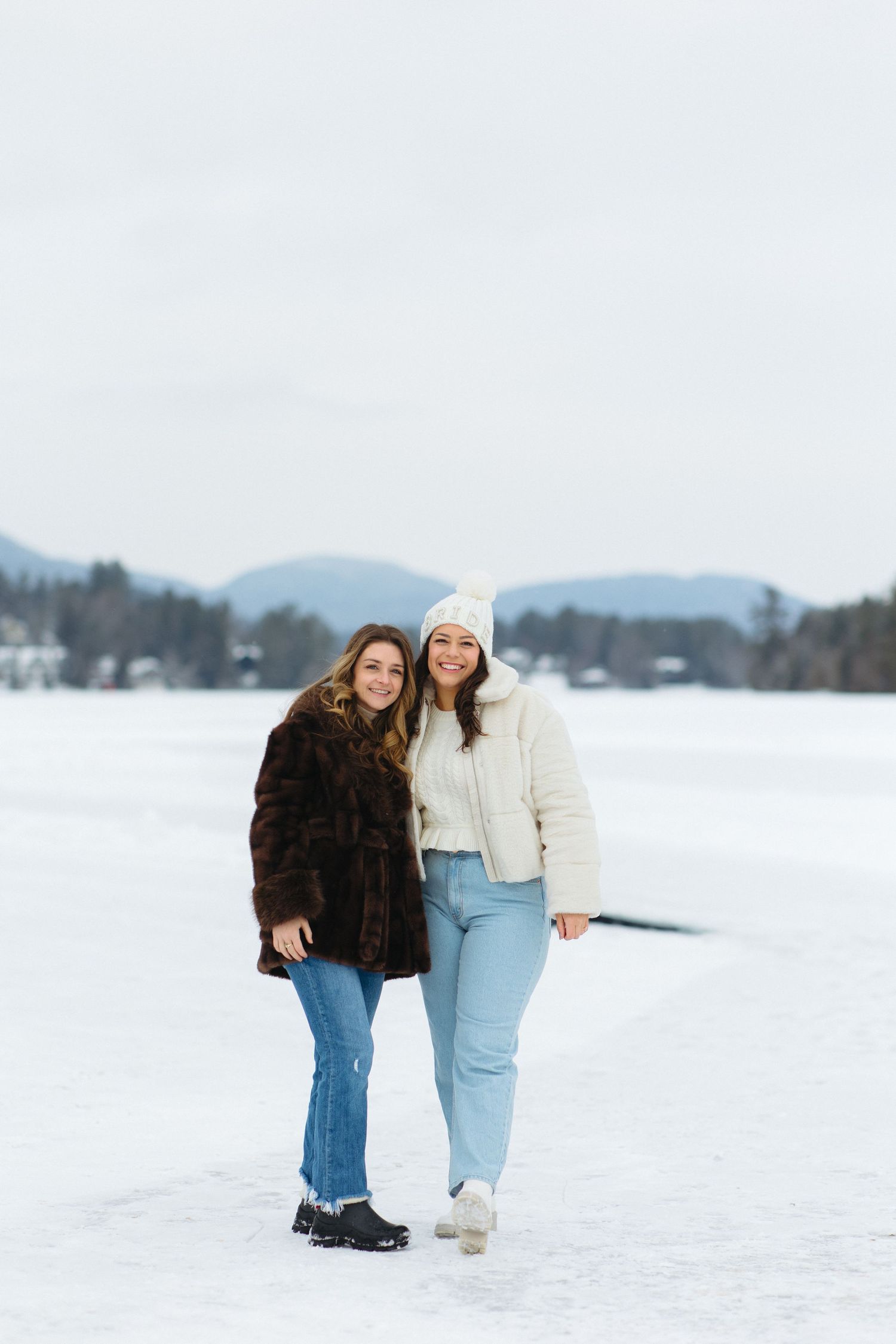 Two friends walking and laughing together in a snowy winter landscape wearing cozy outfits.