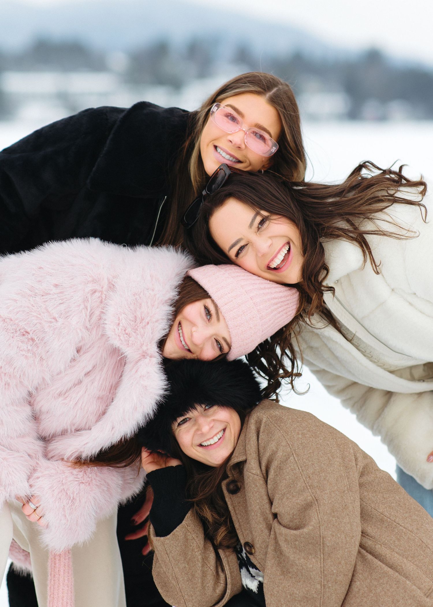 Friends having fun and laughing while posing together in winter coats against a snowy backdrop.