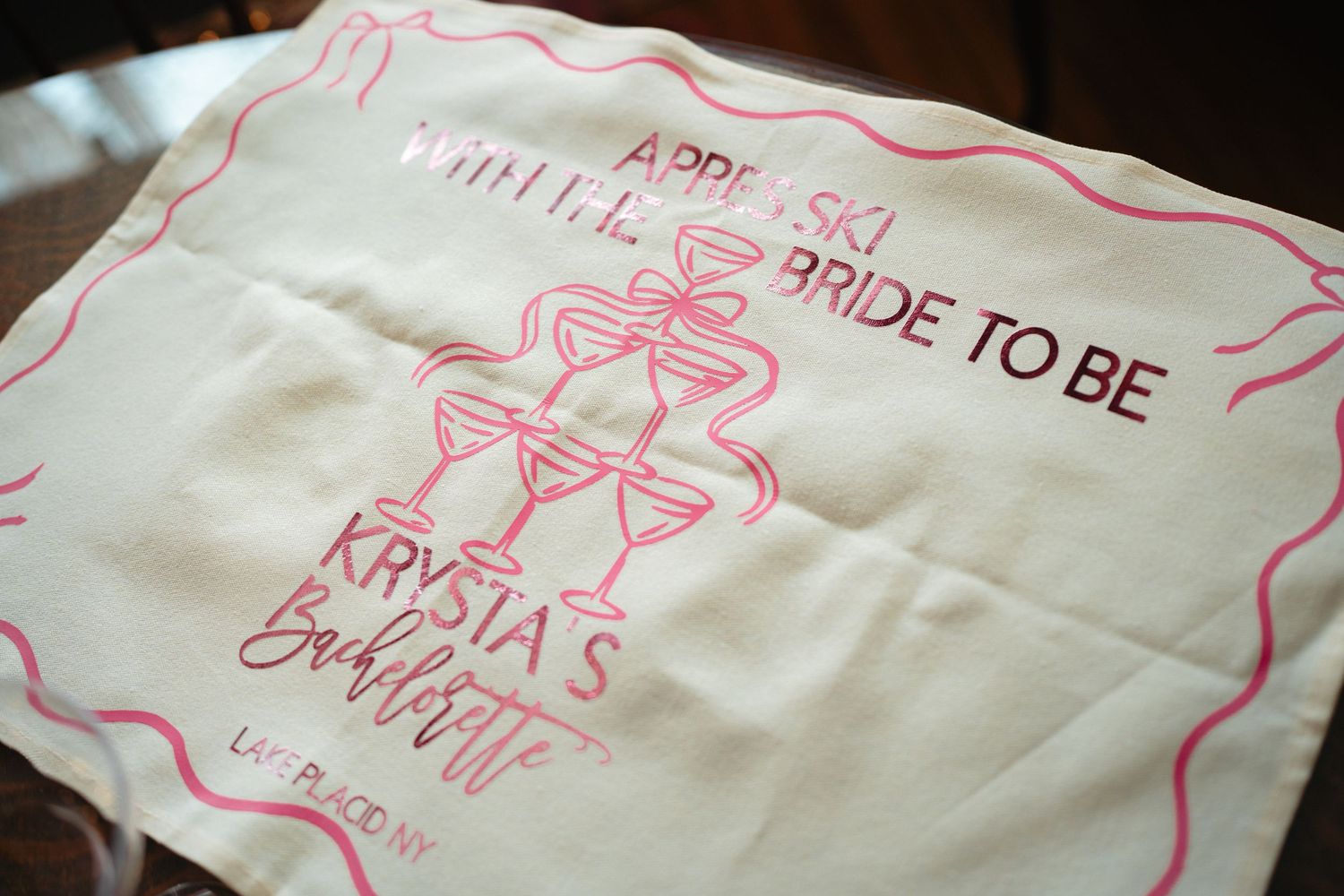 A white napkin with pink text and graphics for a bridal shower party featuring champagne glass designs.
