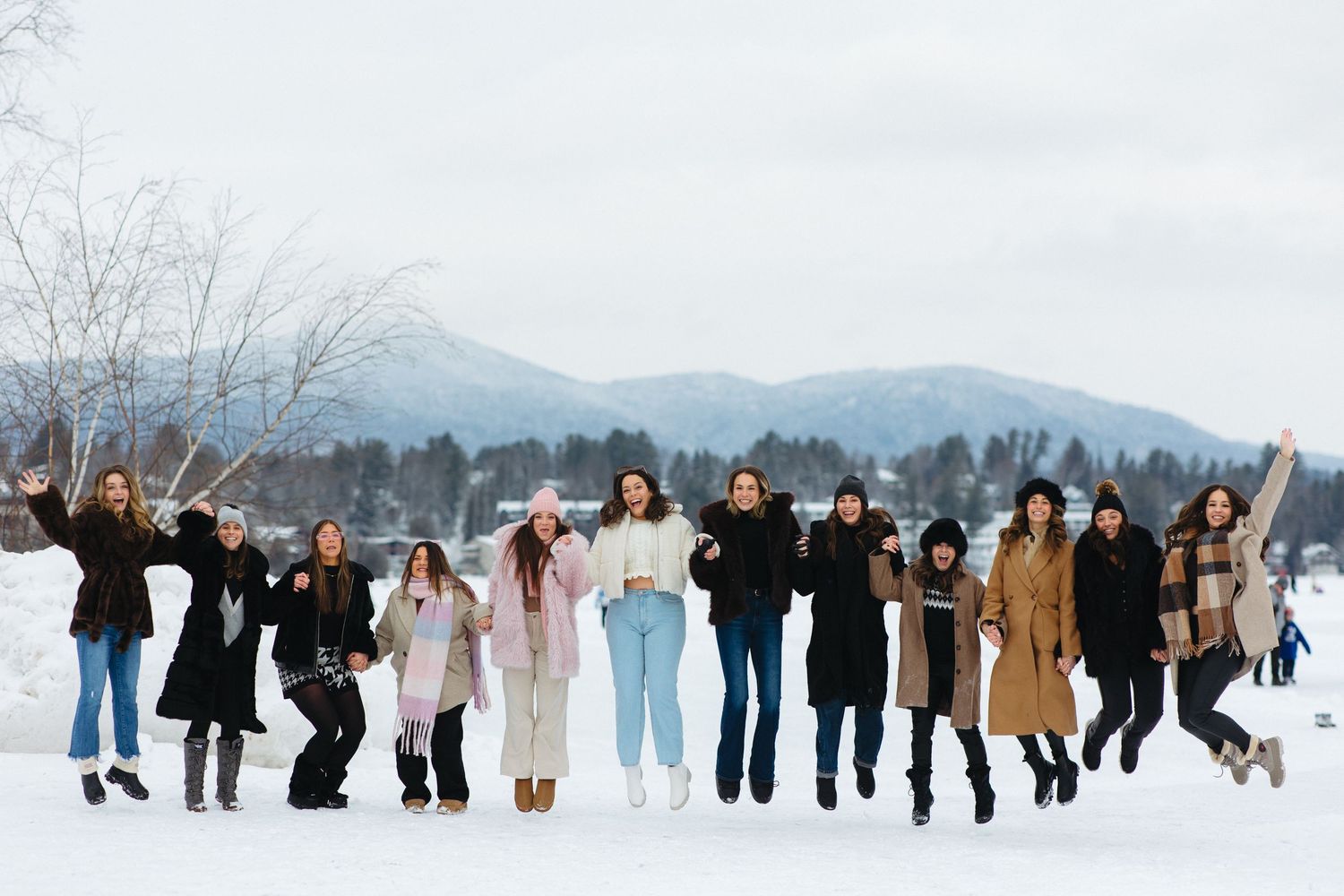 Large group jumping together in the snow with mountains visible in the background.