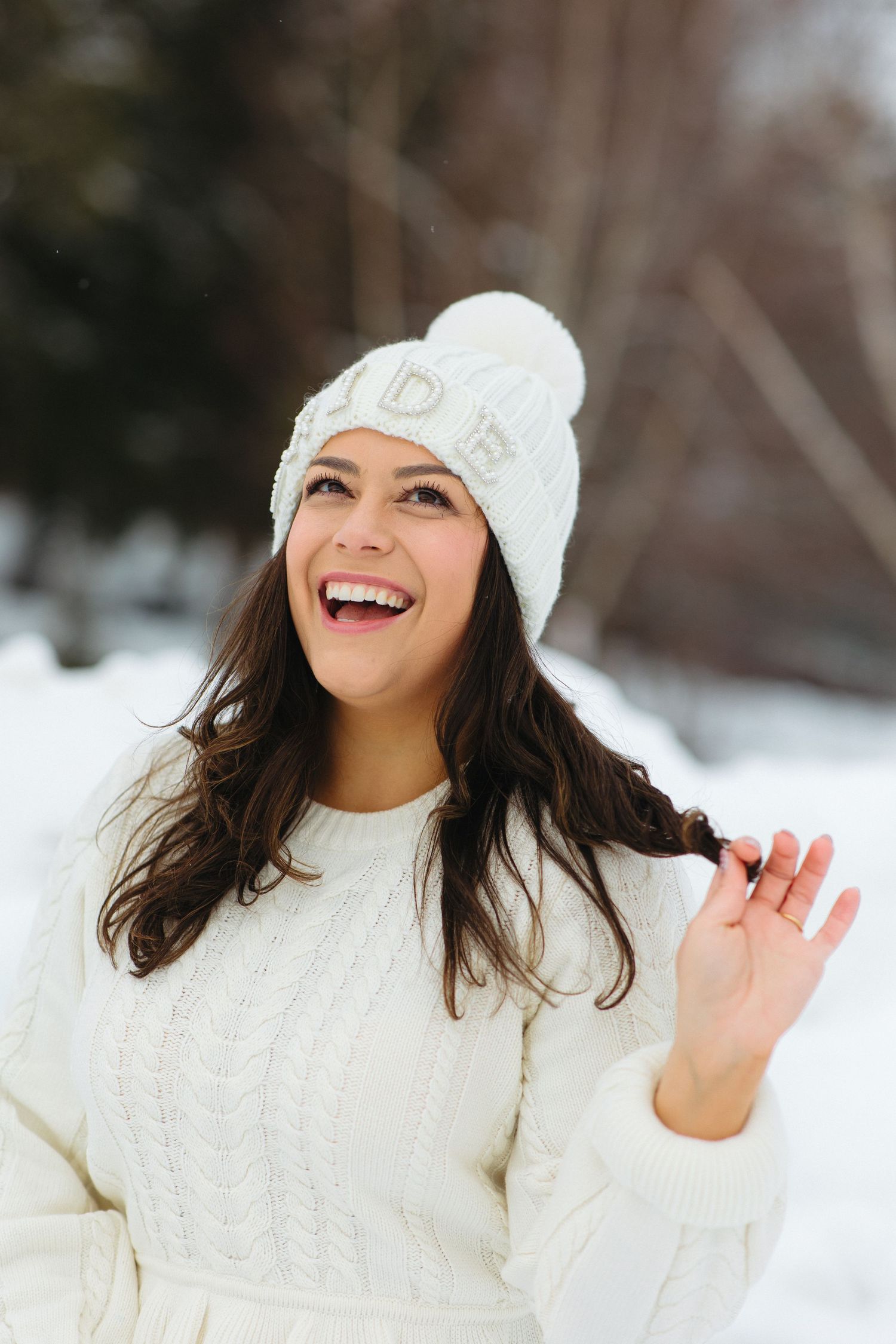 Person wearing a white knit sweater and beanie hat laughing joyfully in a winter snow scene.