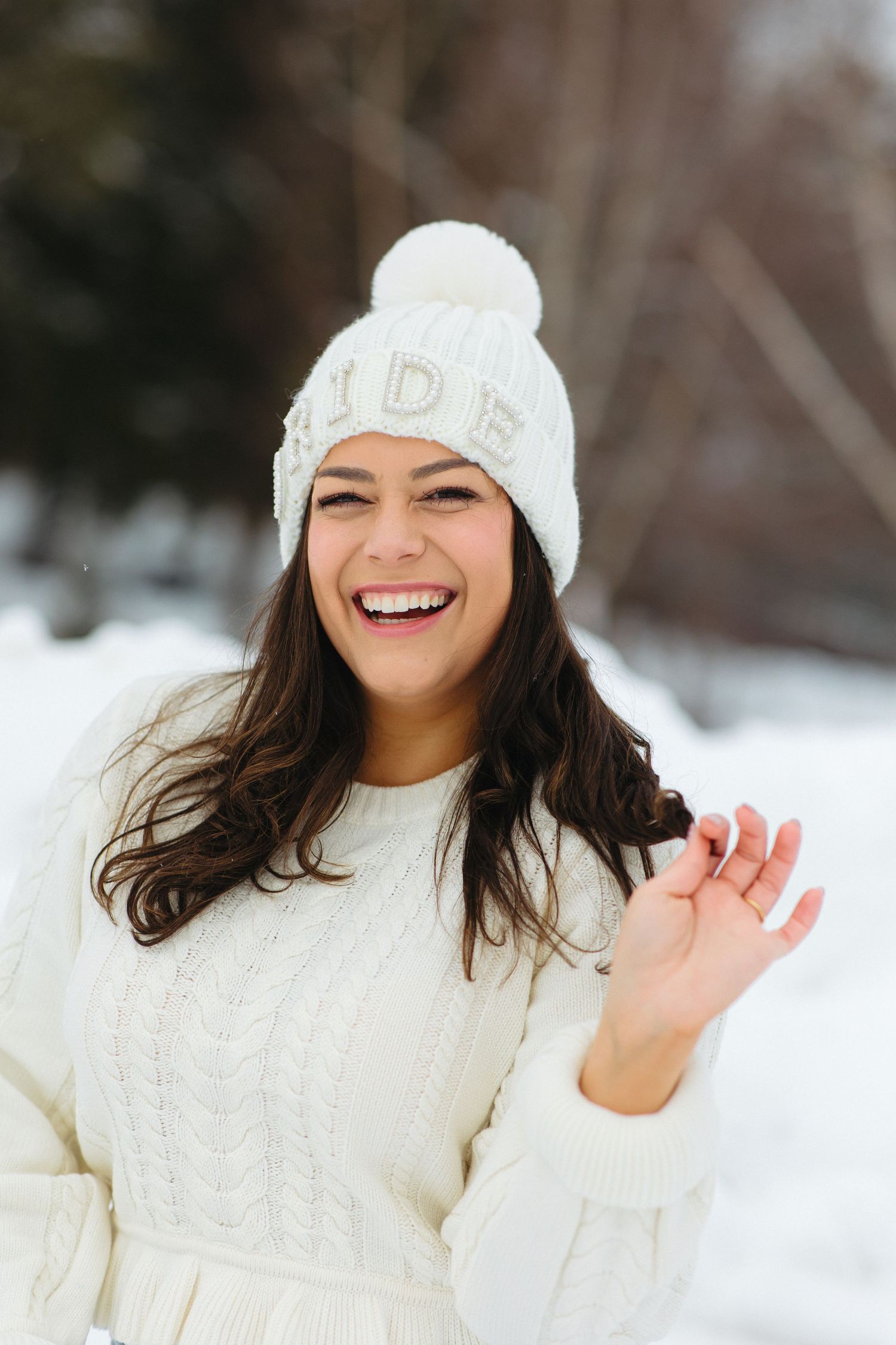 Person in white winter attire smiling and waving in snowy setting.