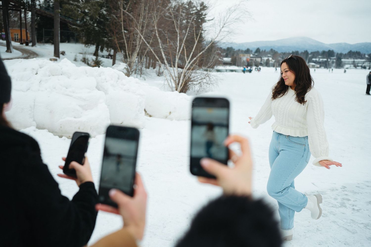 Behind-the-scenes photo of people taking pictures with phones of someone jumping in the snow.