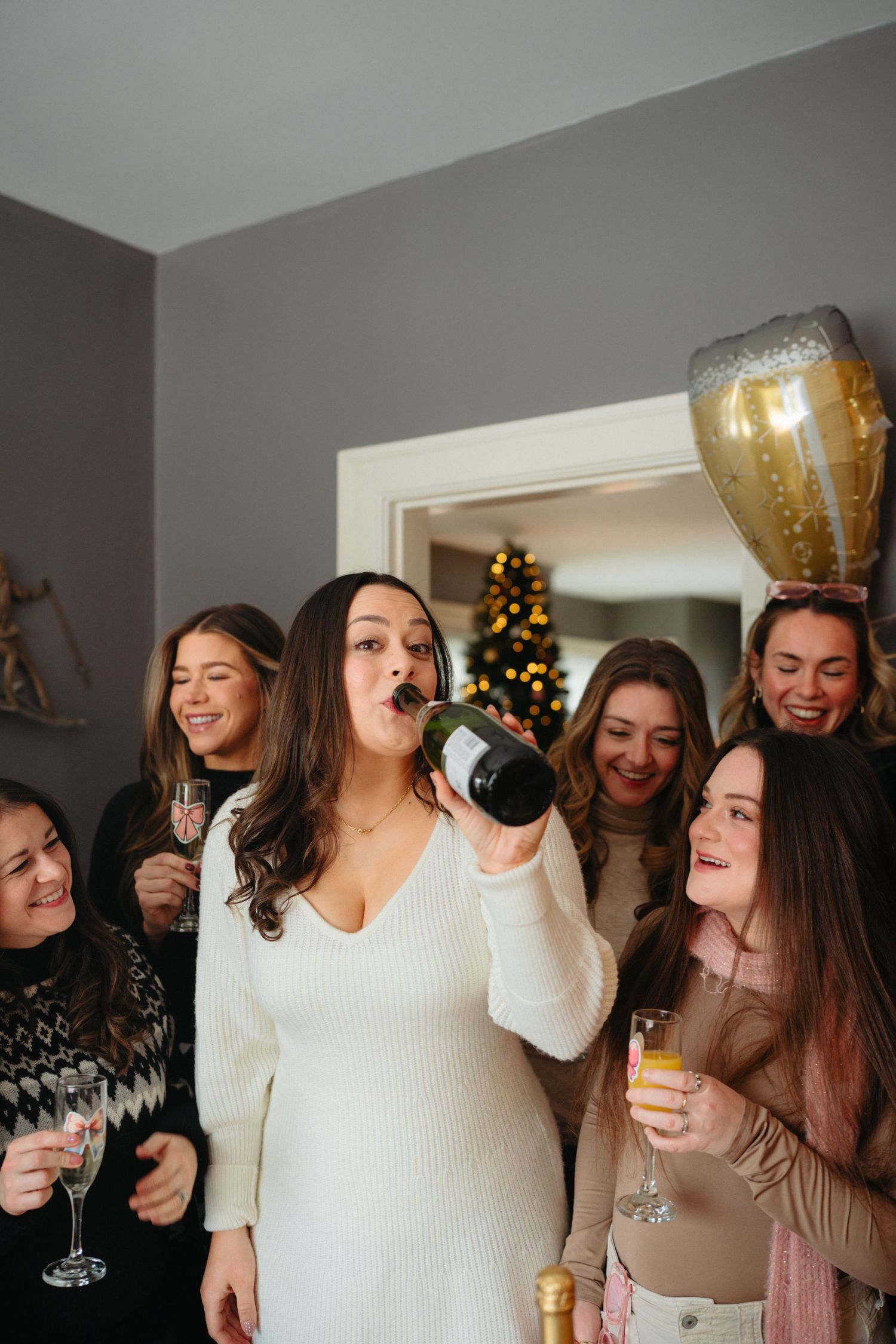 A group of friends enjoying drinks and celebrating during the holiday season with a Christmas tree in the background.