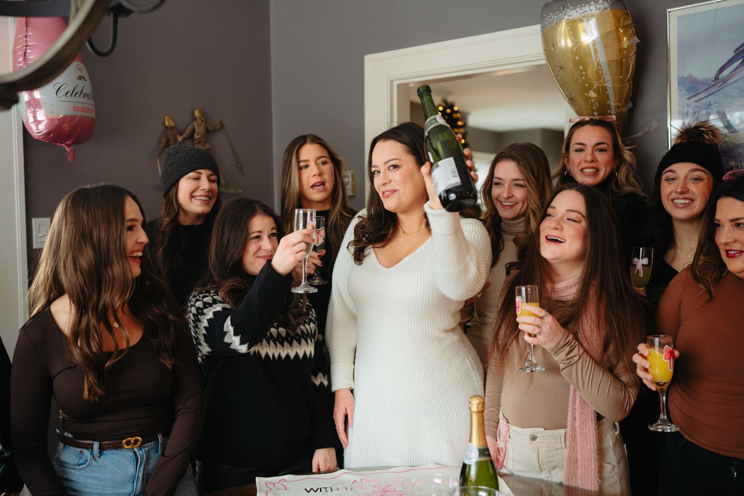 A group celebrates together in a festive indoor setting with balloons and a trophy in the background.