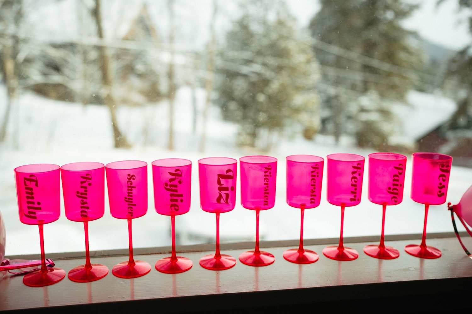 Pink plastic wine glasses arranged in a long row on a white surface against a snowy winter background.