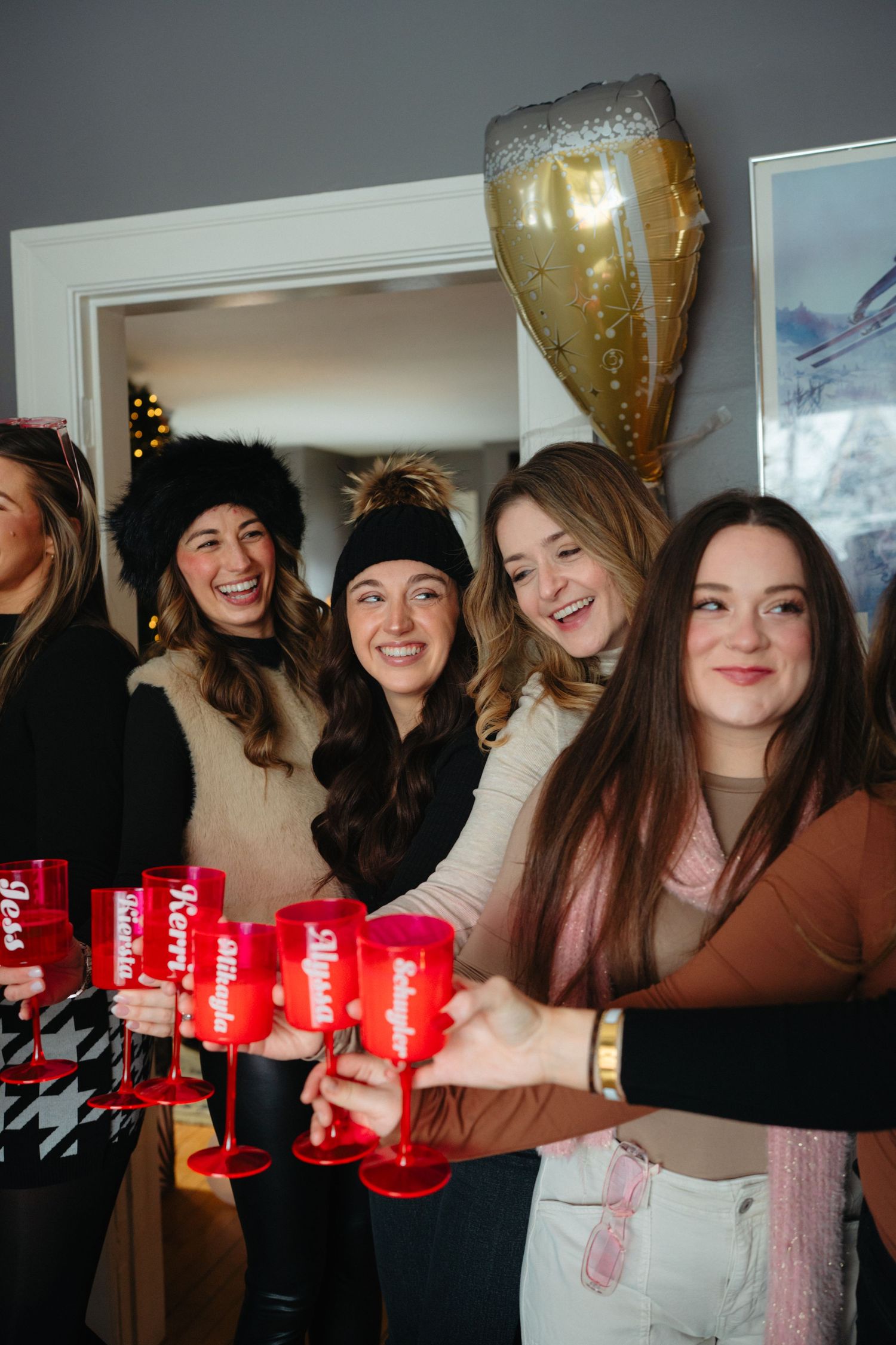 Group of friends celebrating with red cups and gold balloons at an indoor party.