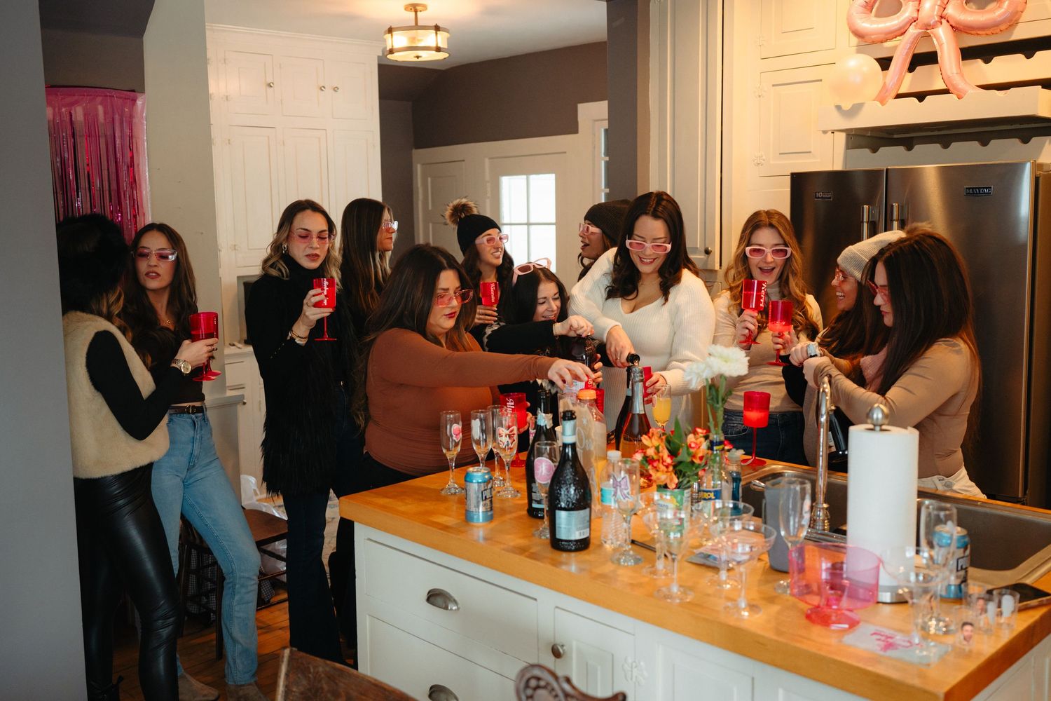 People gathered around a kitchen counter with drinks and party decorations.
