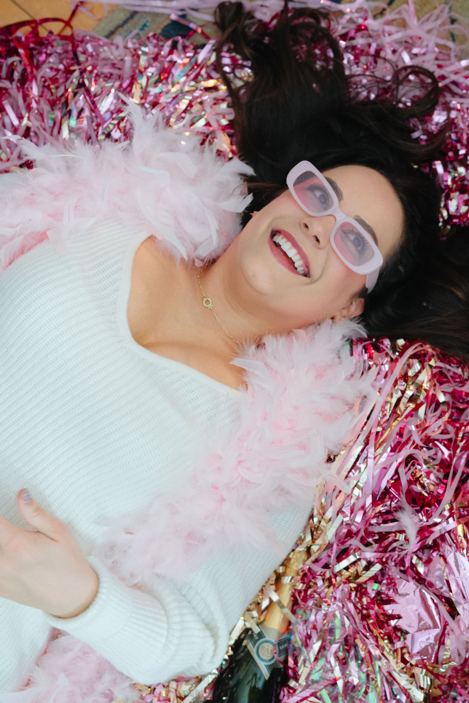 Person lying on floor surrounded by pink metallic tinsel and party decorations.