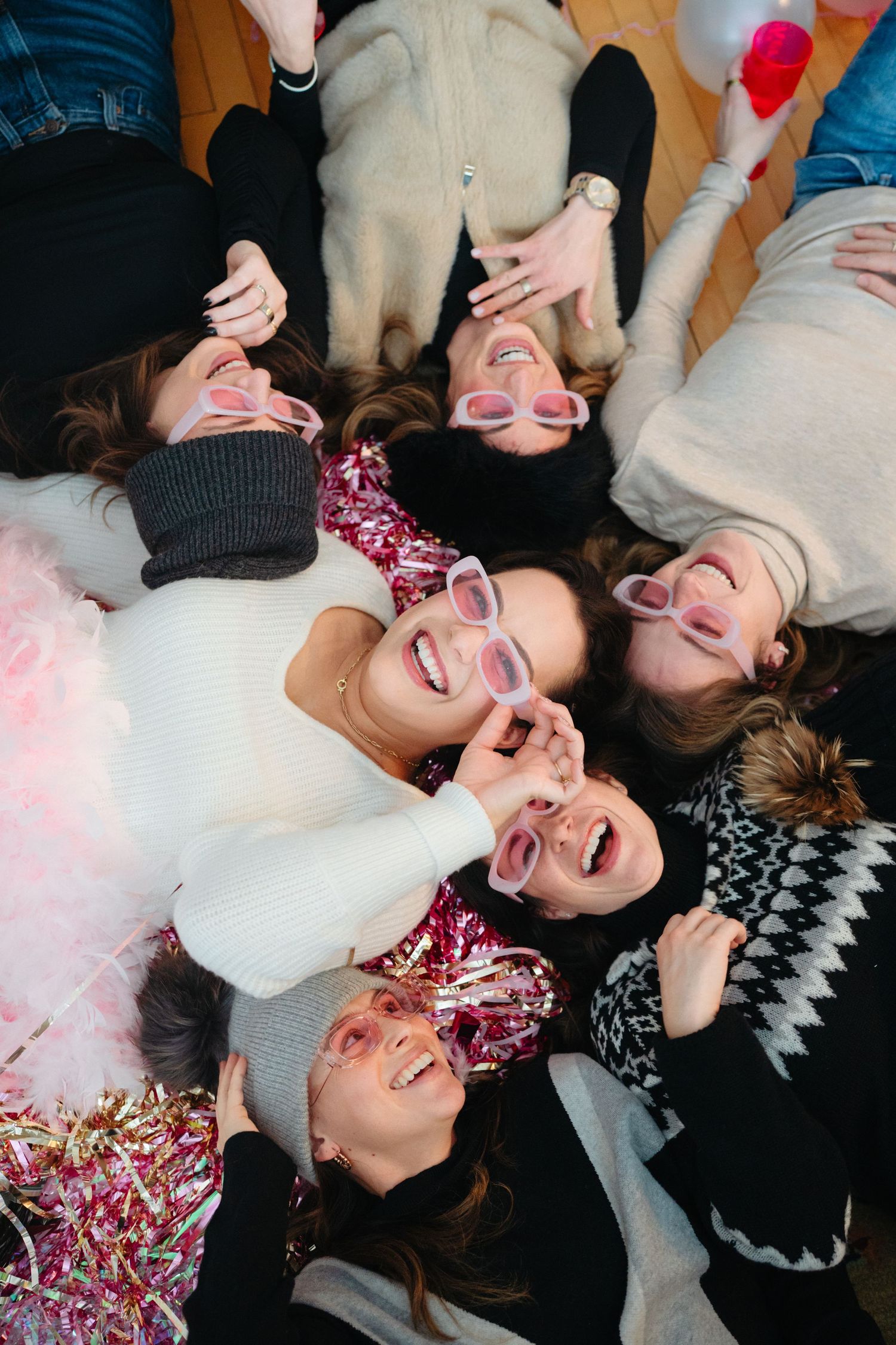 A group of friends lying down together laughing joyfully while wearing casual winter attire.