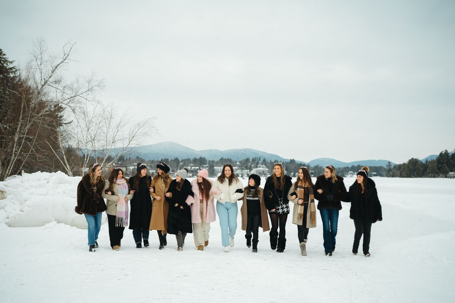 A group stands together in winter coats against a snowy mountain landscape backdrop.