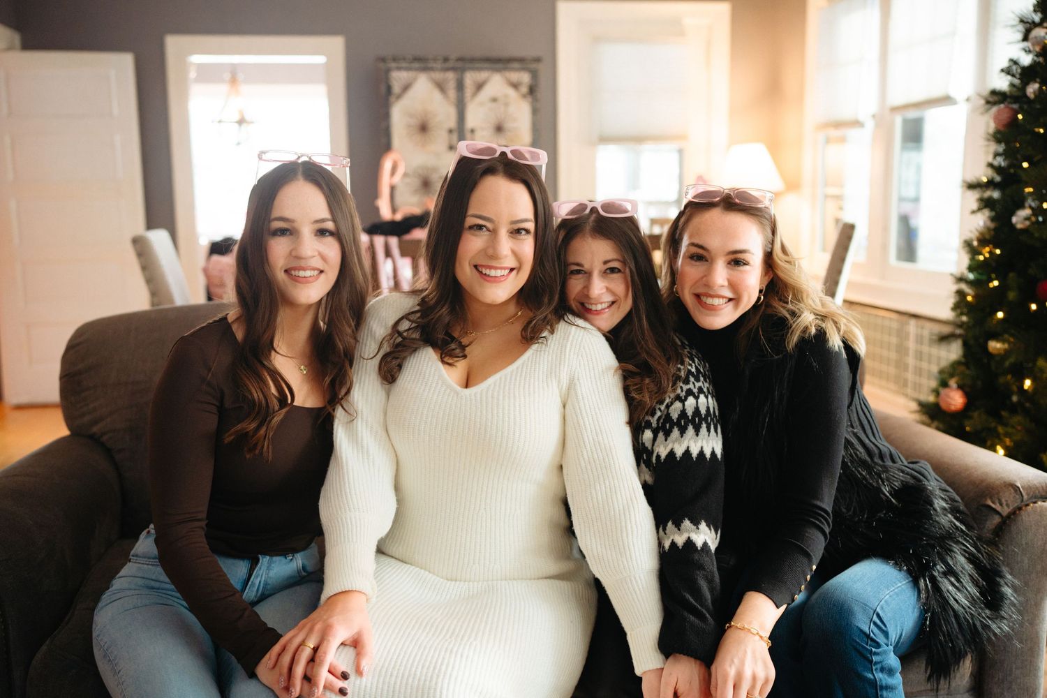 A group of people gather together in a cozy living room with holiday decorations and a Christmas tree.